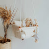 Cuddle bunny sitting in beige baby swing with white ropes and wooden dowels.