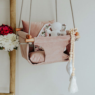 Cuddle bunny sitting in Blush pink velvet baby swing with grey ropes and wooden dowels.